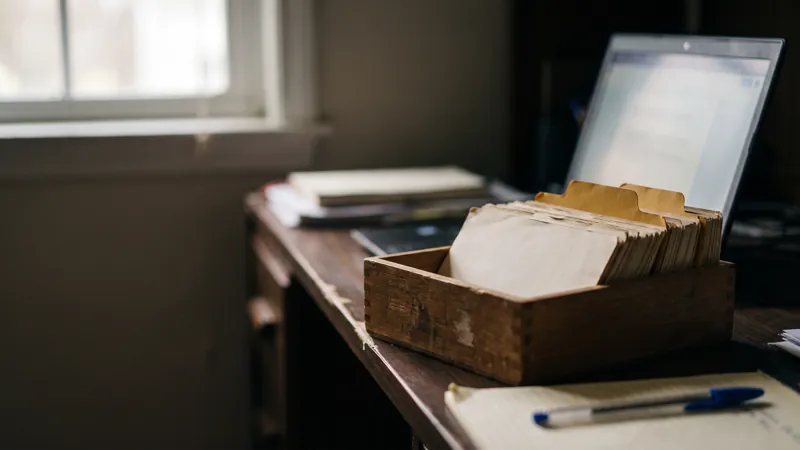 Ancien fichier clients en bois avec intercalaires jaunes devant un ordinateur portable ouvert