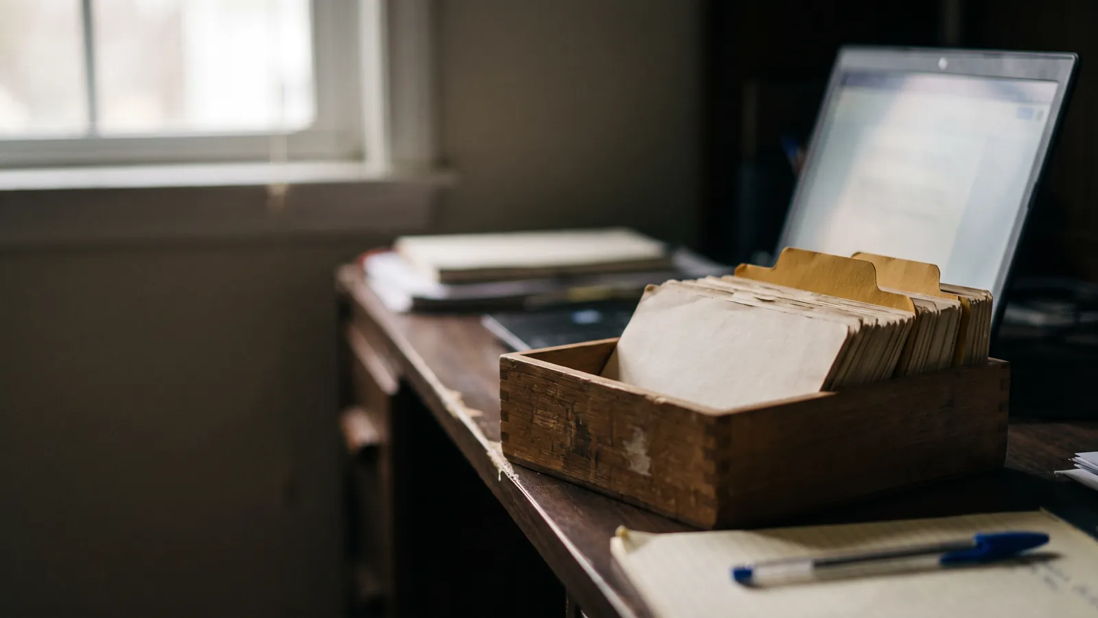 Ancien fichier clients en bois avec intercalaires jaunes devant un ordinateur portable ouvert